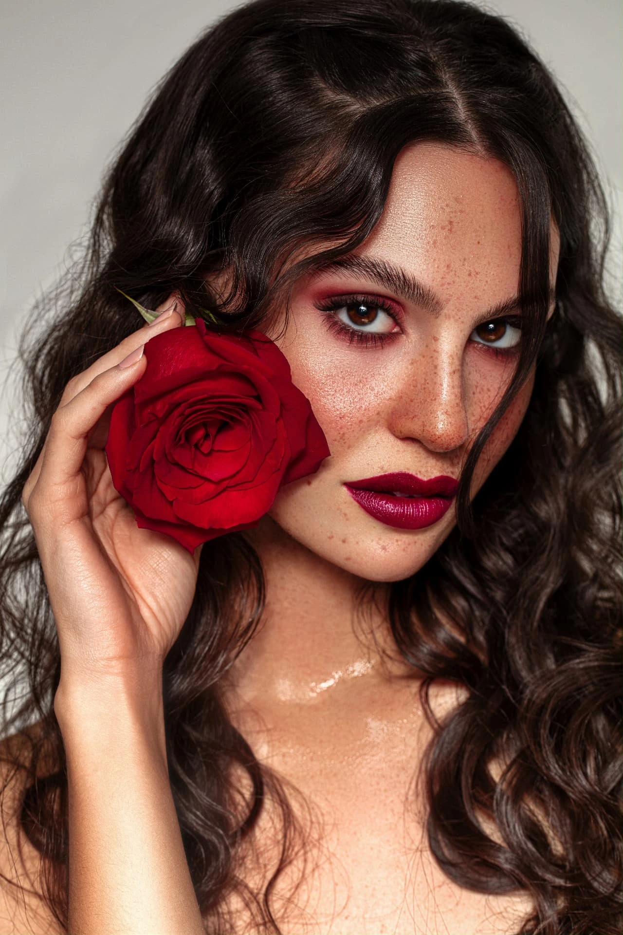 Make-up bordeaux con labbra rosse e una rosa accanto al volto
